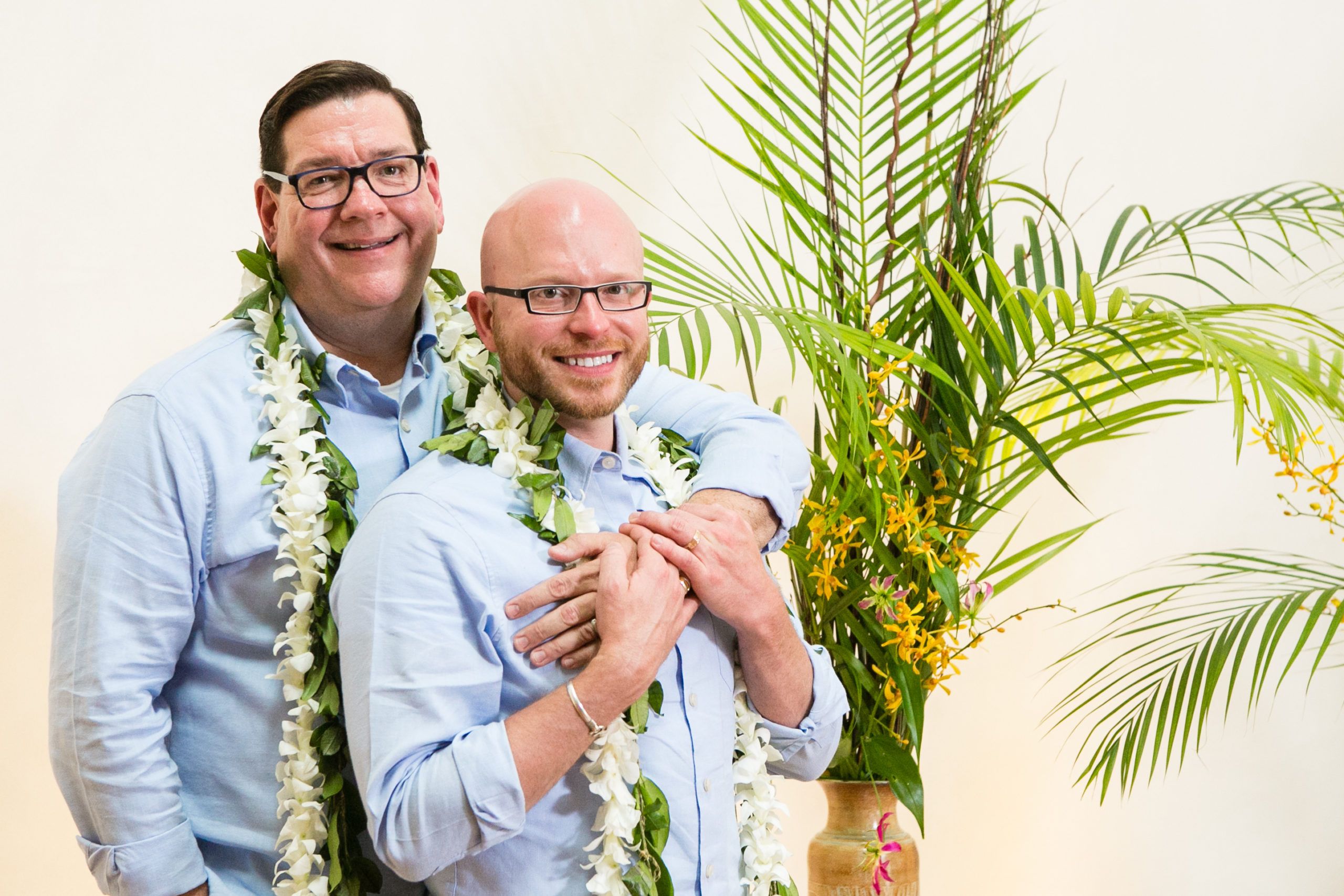Two grooms wear white and green tropical leis | PartySlate