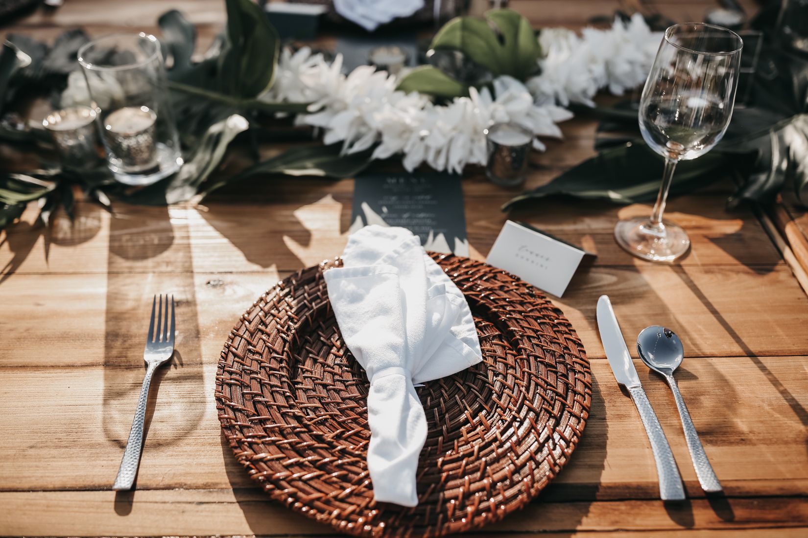 Tropical reception table with wicker charger plate, white napkin, and white orchid centerpiece with greenery | PartySlate