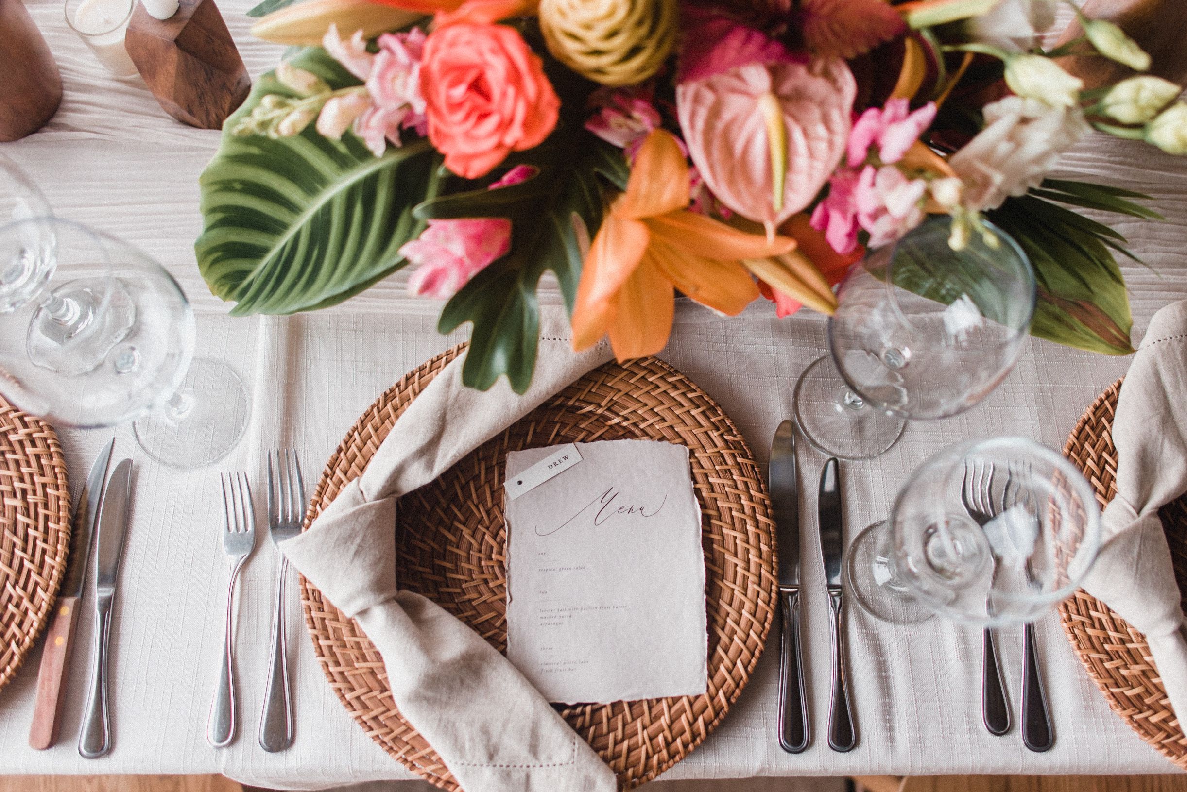 Tropical tablescape with bright flowers and wicker plate charger | PartySlate