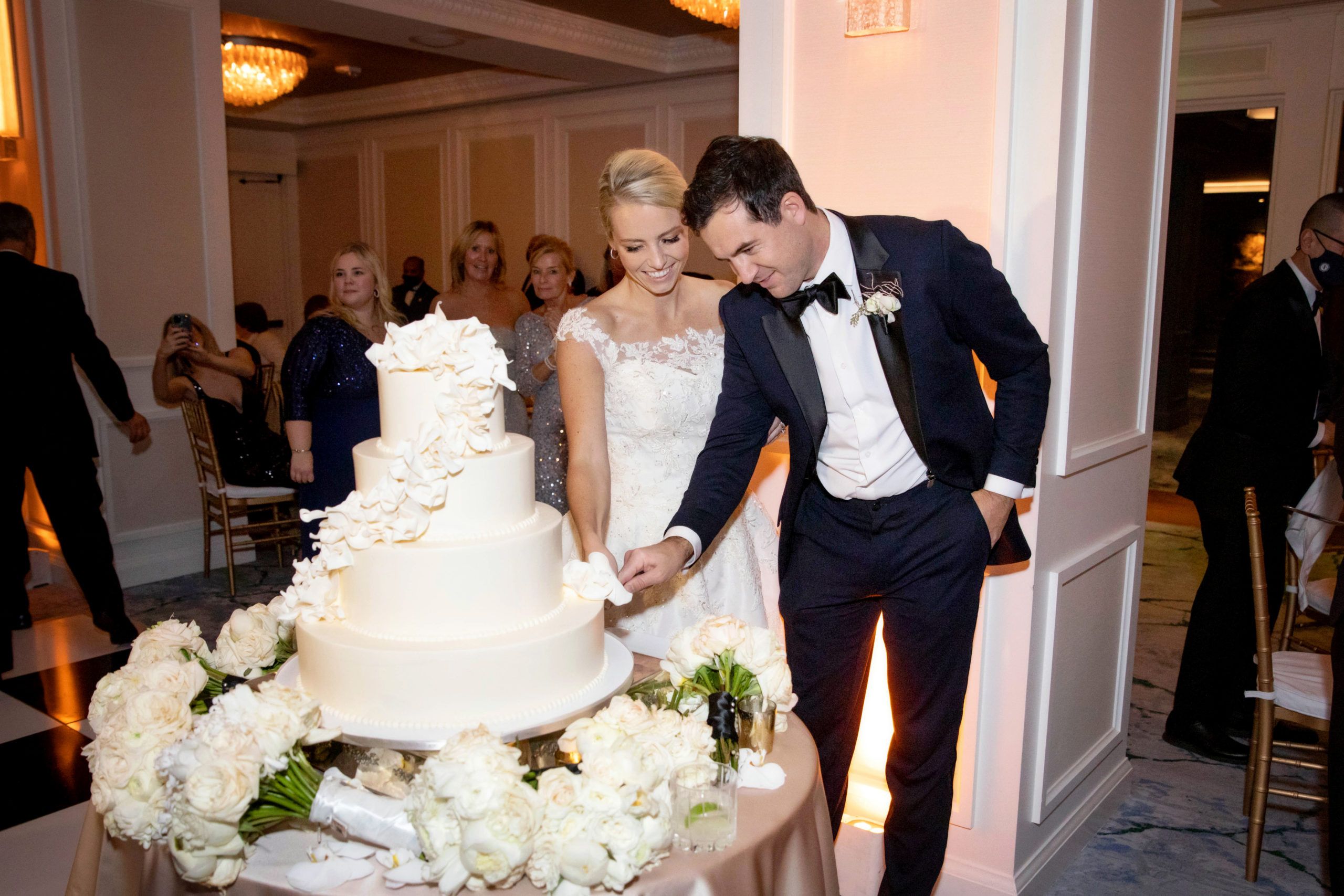 Couple cutting into their white wedding cake with a little bit of greenery on it | PartySlate
