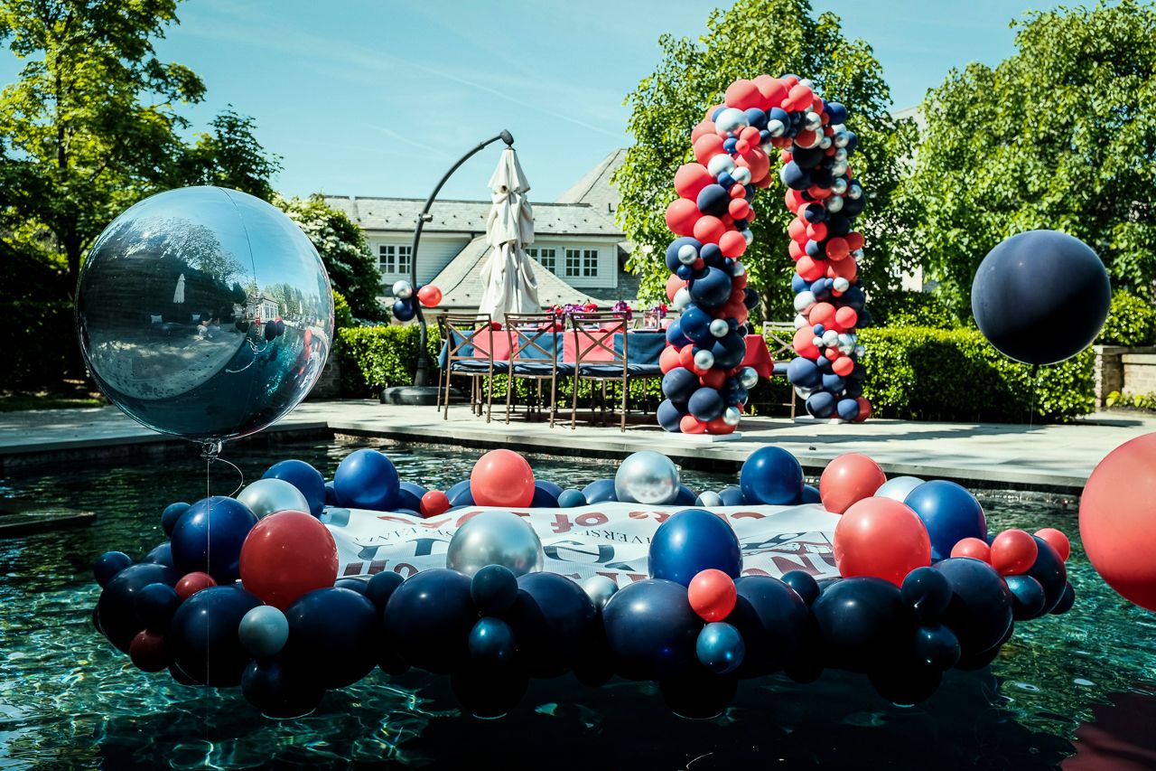 balloon arch next to a backyard pool and balloons in the pool | PartySlate
