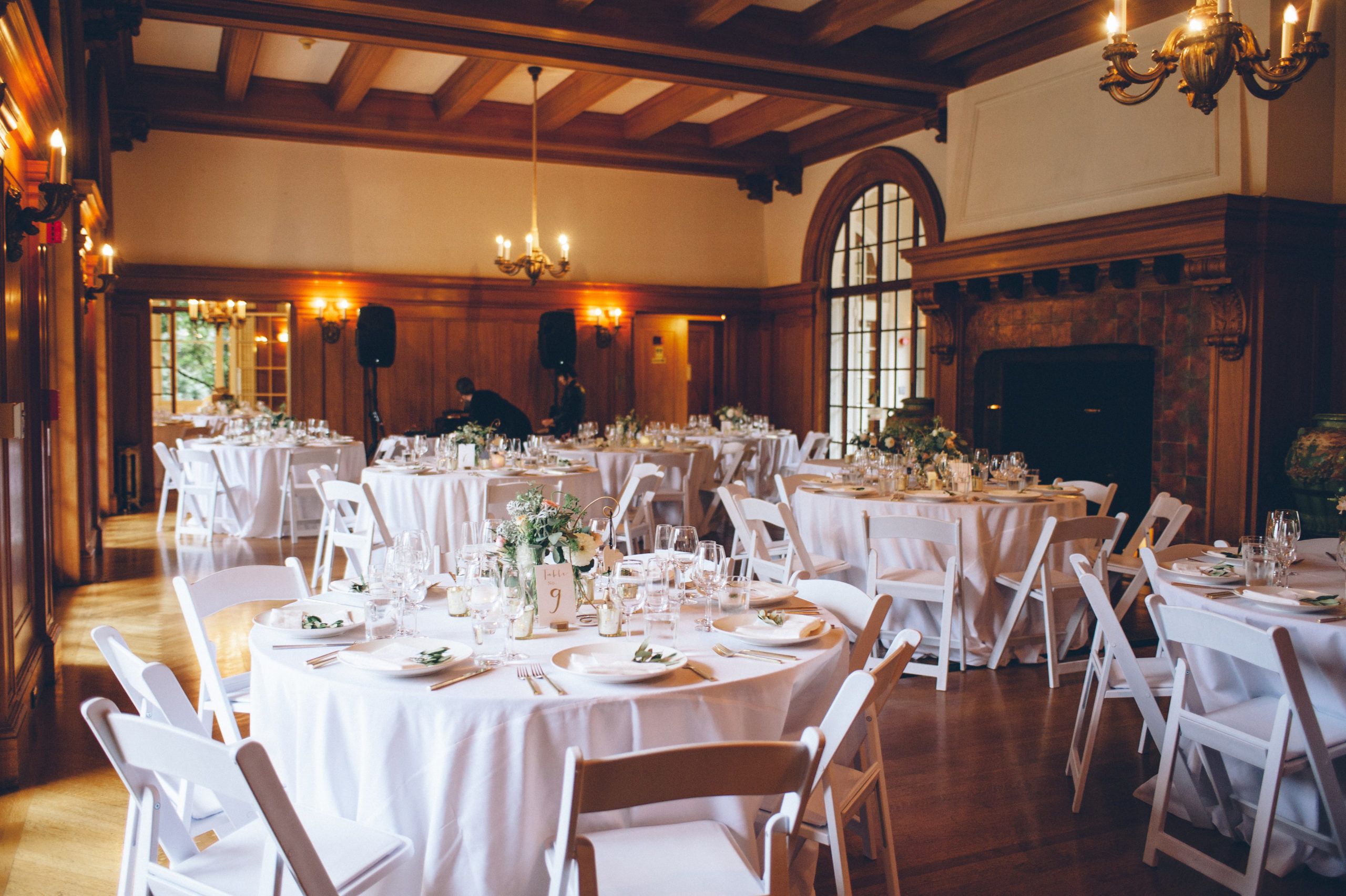 Reception hall with round tables in white table cloths and dark wood accents around the room | PartySlate
