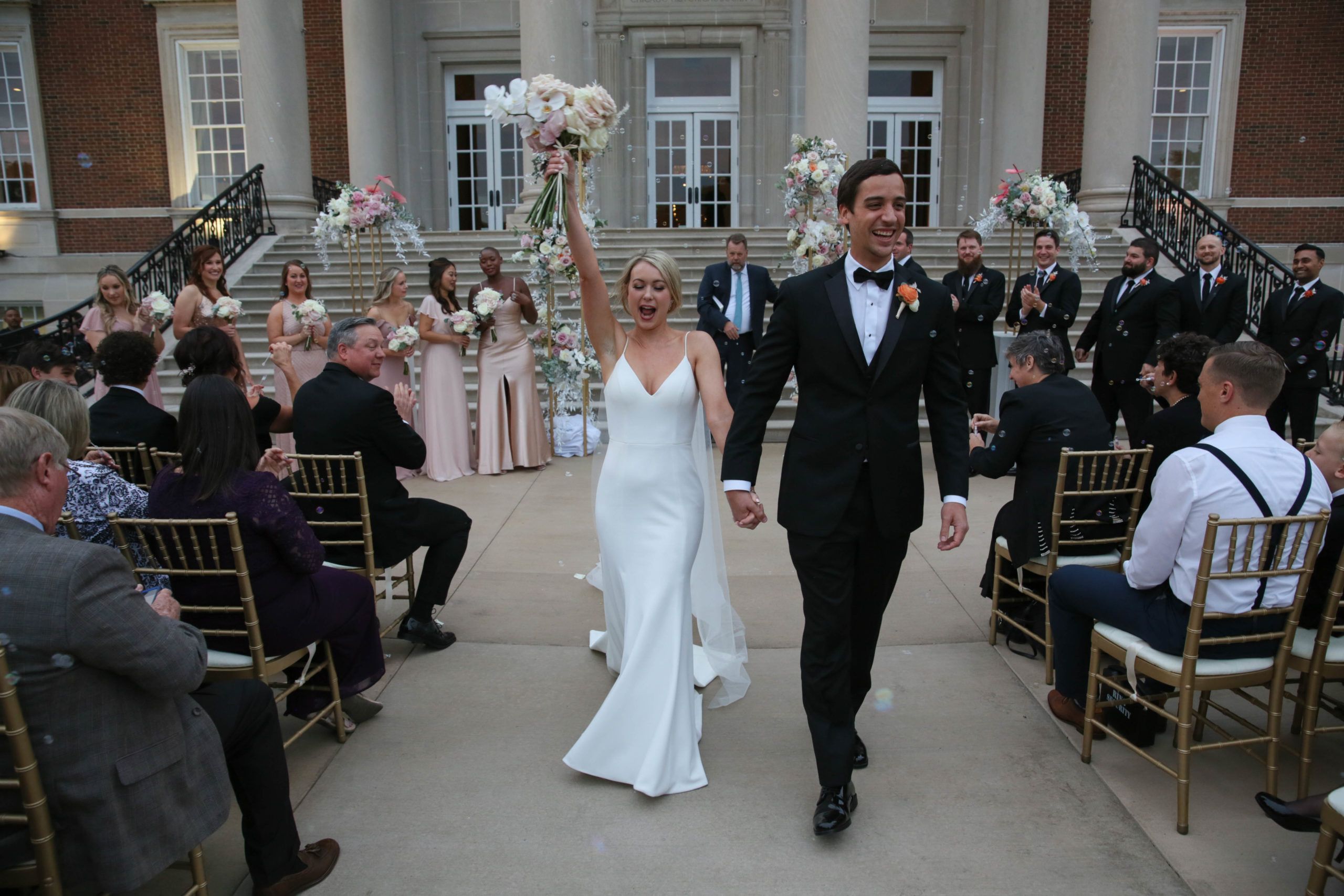 couple walking down aisle at outdoor chicago wedding with white and pink florals | PartySlate