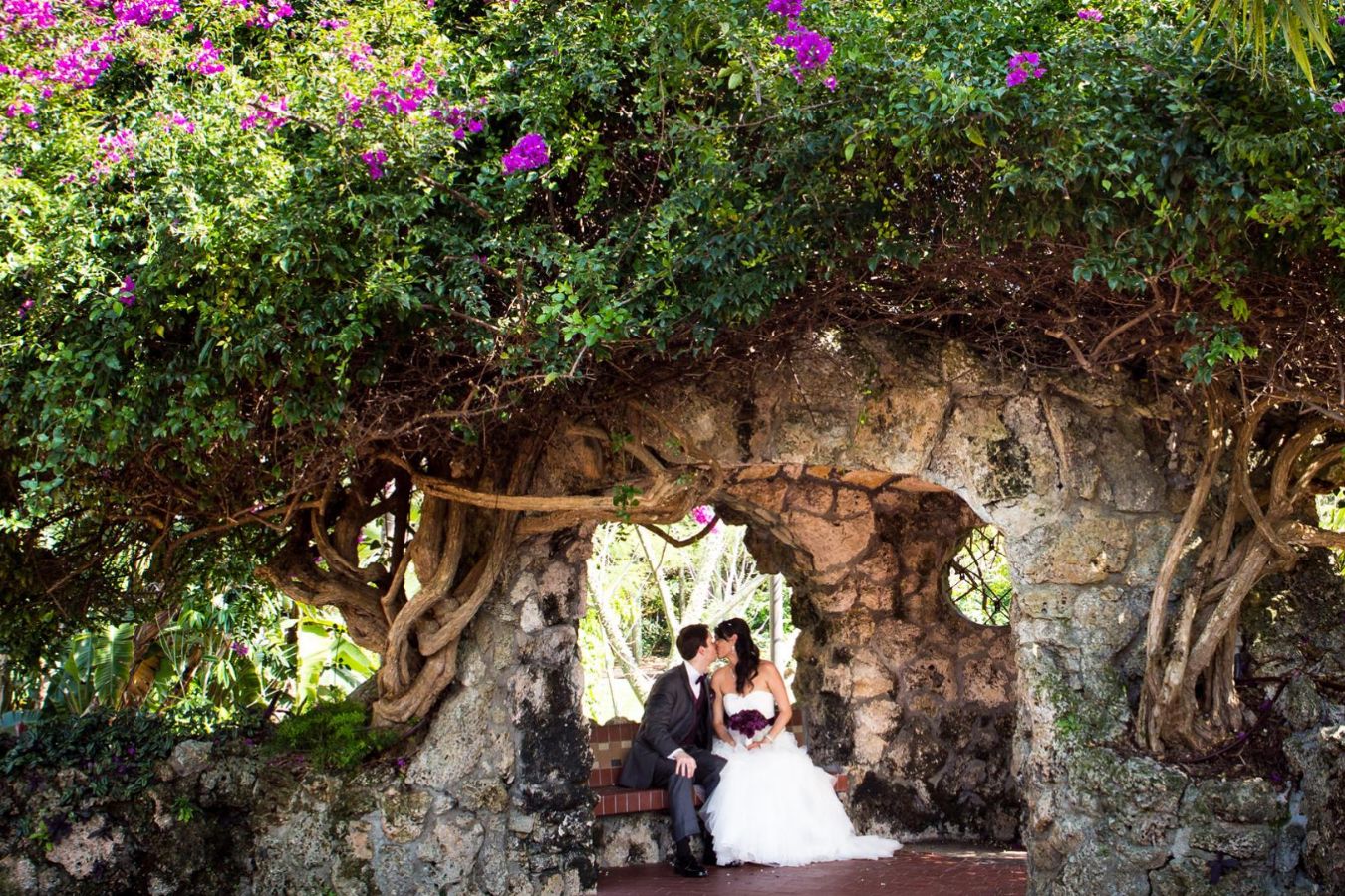wedding at Pinecrest Gardens in miami with couple sitting in garden inside rock cave | PartySlate