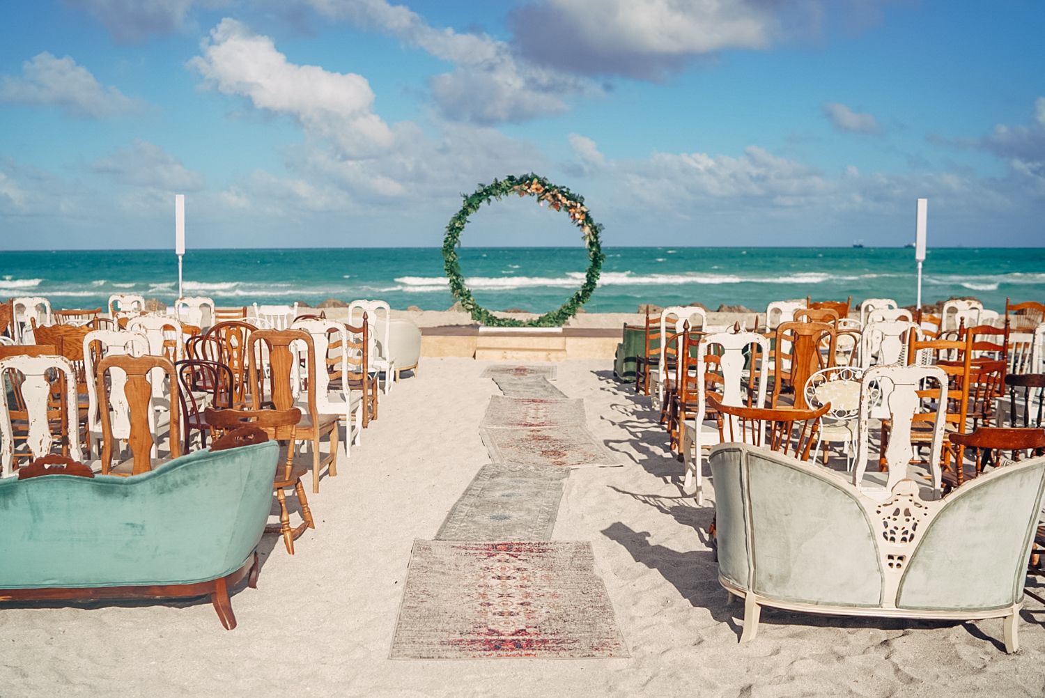 eclectic beach wedding with wedding aisle lined with different style seating and arch at the end | PartySlate