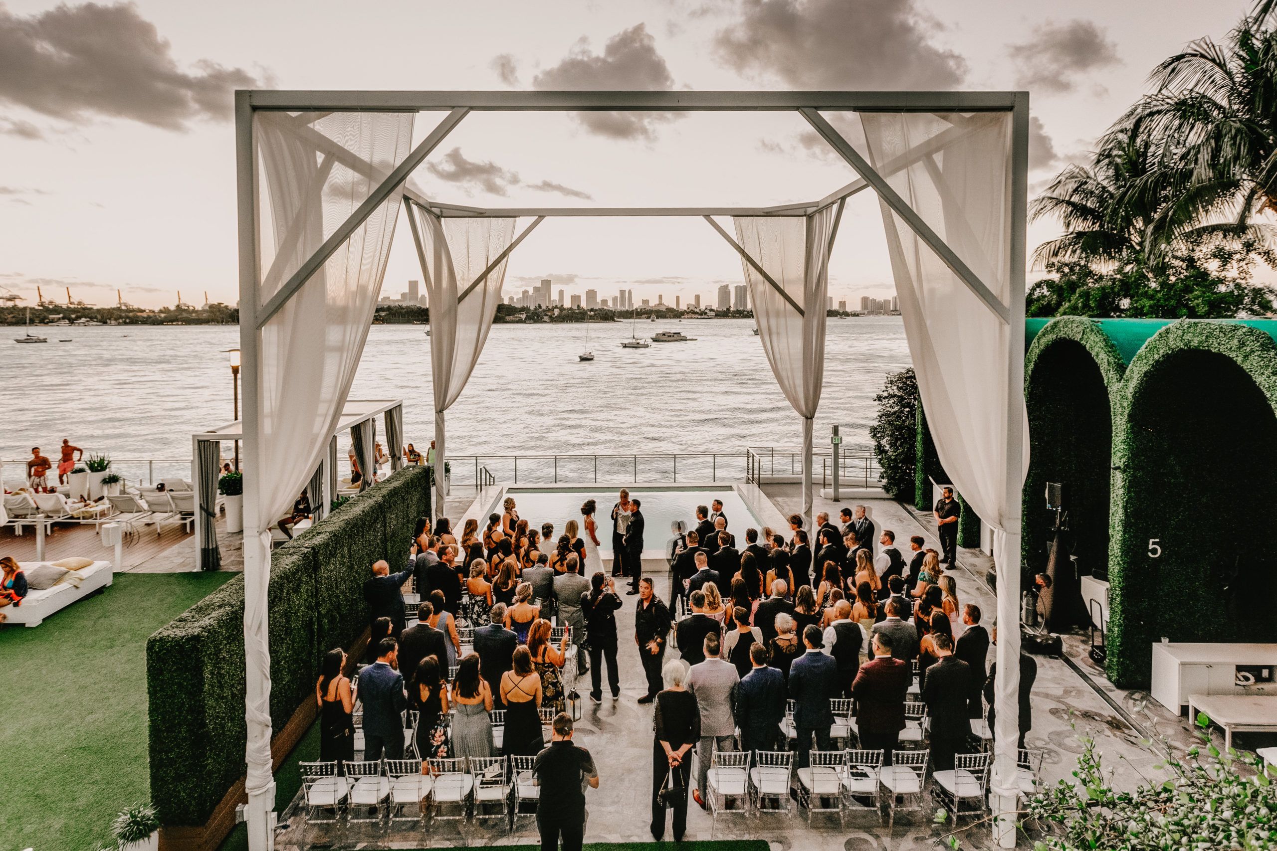 all white outdoor wedding at Mondrian South Beach with couple standing at the alter in front of the ocean with guests around | PartySlate