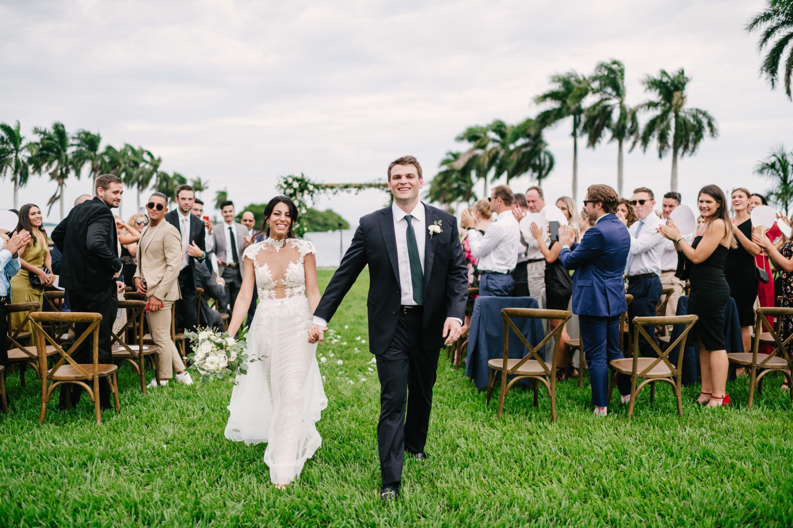 outdoor wedding in miami with coupld walking down the aisle together with guests and palm trees behind them | PartySlate