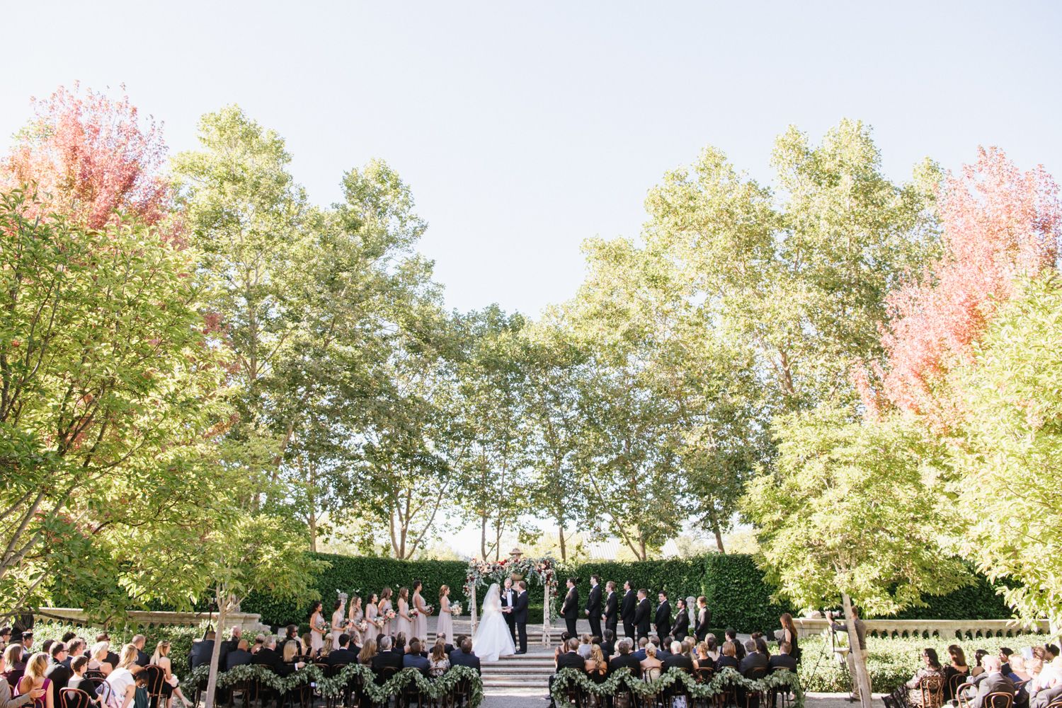 chic wedding in wine country with trees surrounding alter and wedding party | PartySlate