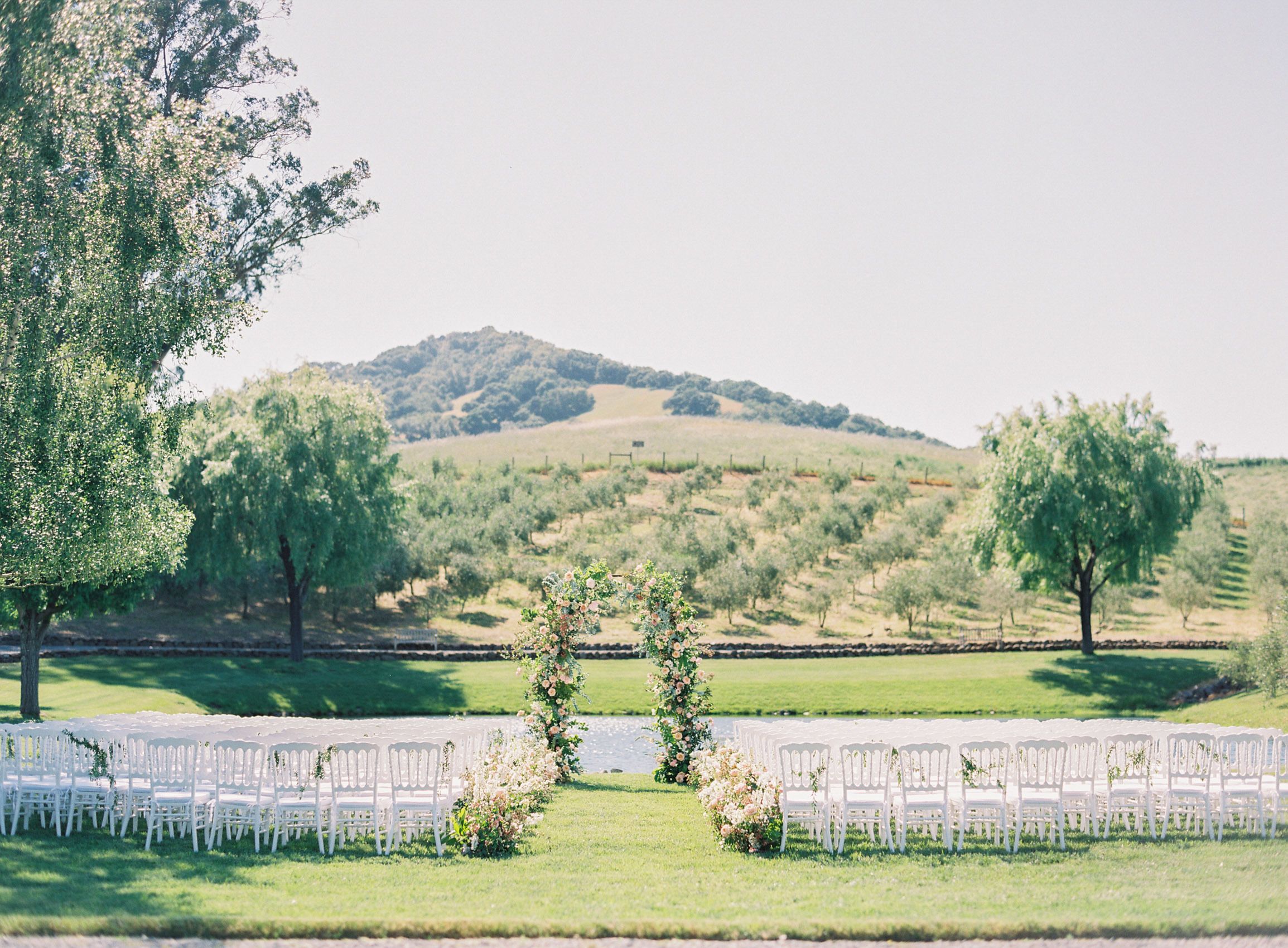 wedding aisle with pond and hills with vineyards behind and floral wedding arch | PartySlate