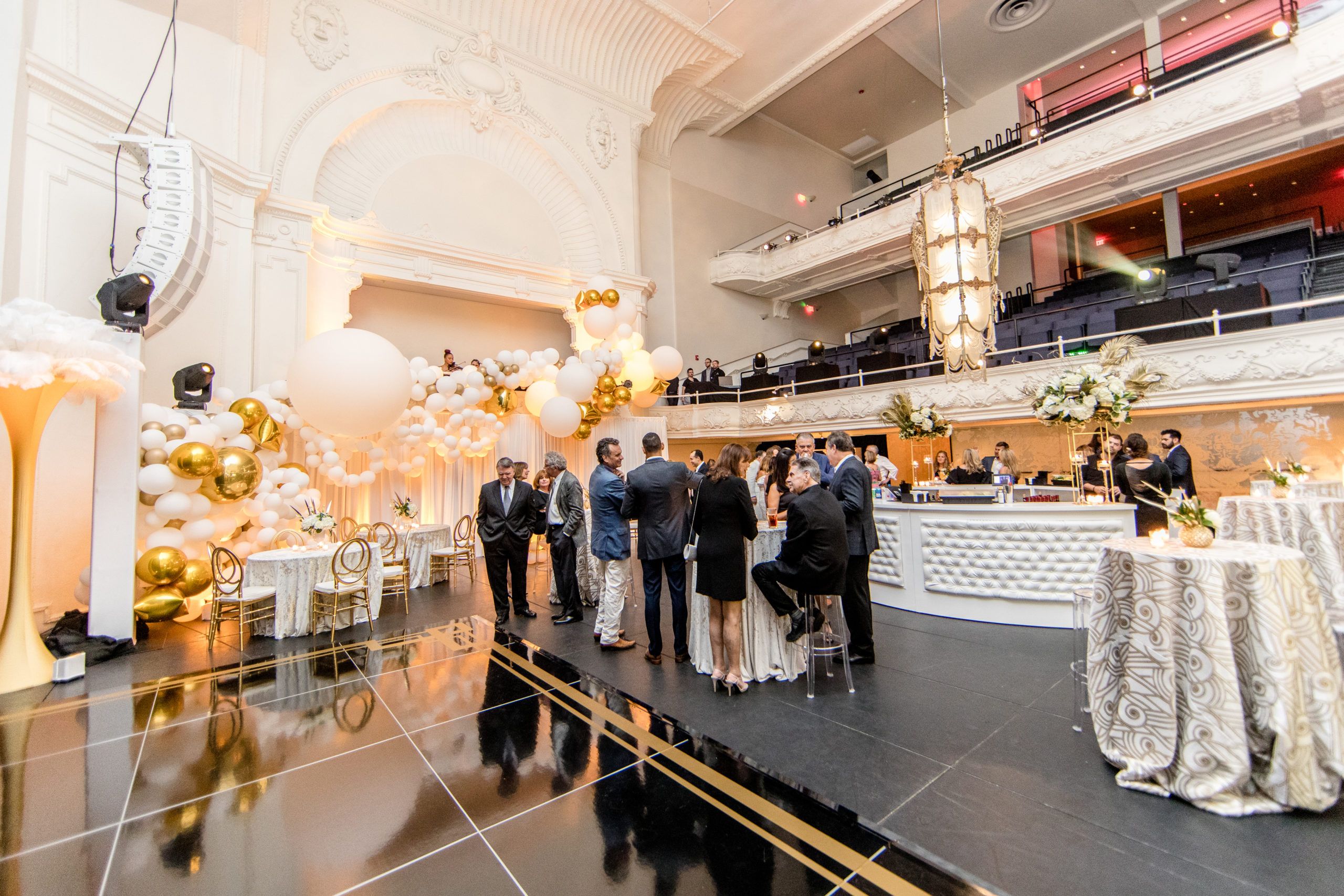 gold and white birthday party with guests standing and eating | PartySlate