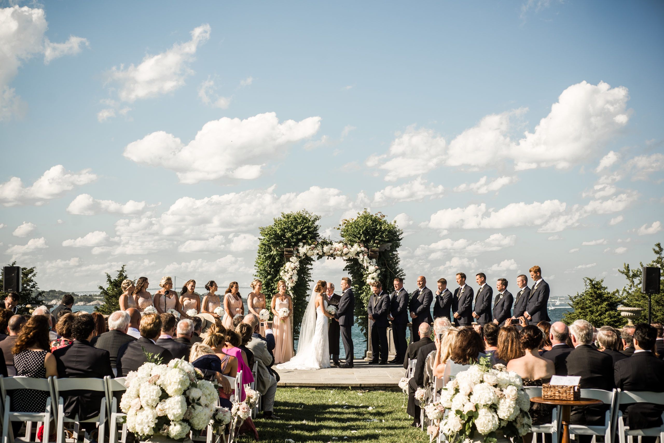Elegant Newport Nuptials at Castle Hill Inn with couple standing at alter with floral arch and guests seated | PartySlate