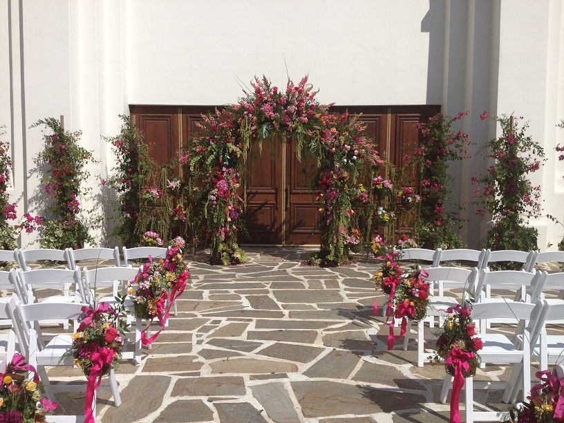 outdoor wedding at Betty H. Reckas Cultural Center with pink floral arch and flowers lining the aisle | PartySlate