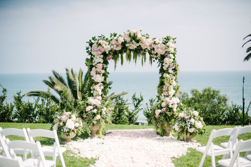 oceanfront outdoor wedding with floral arch and white flower petals on the alter | PartySlate