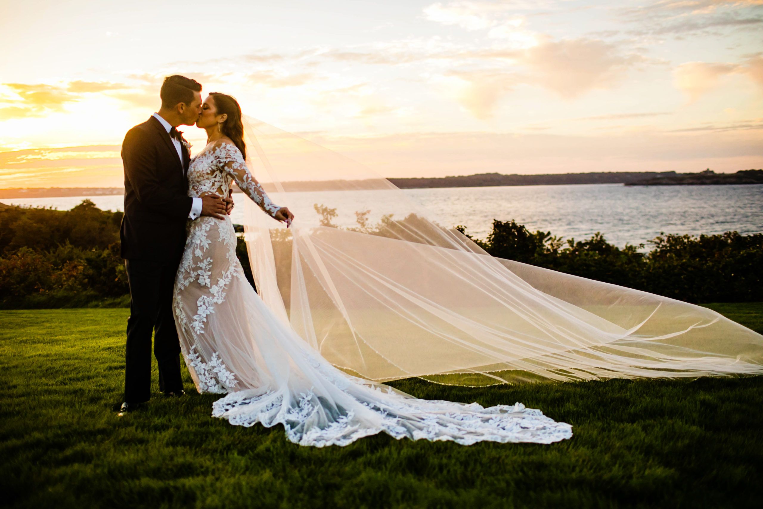 Romantic Wedding at OceanCliff Hotel in Newport, Rhode Island with couple kissing outside with ocean and sunset in the background | PartySlate