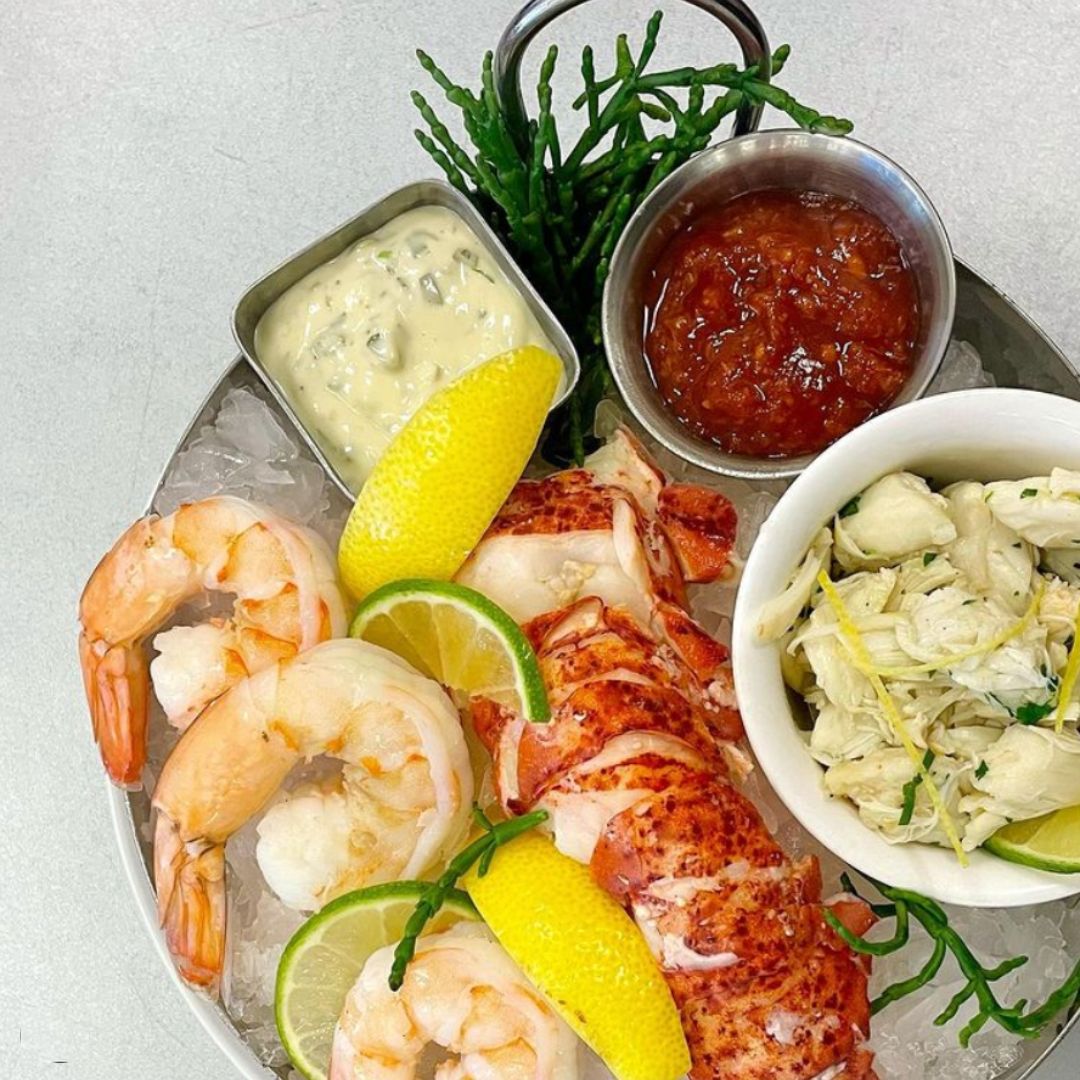A plate full of seafood like shrimp, lobster, and dipping sauces.