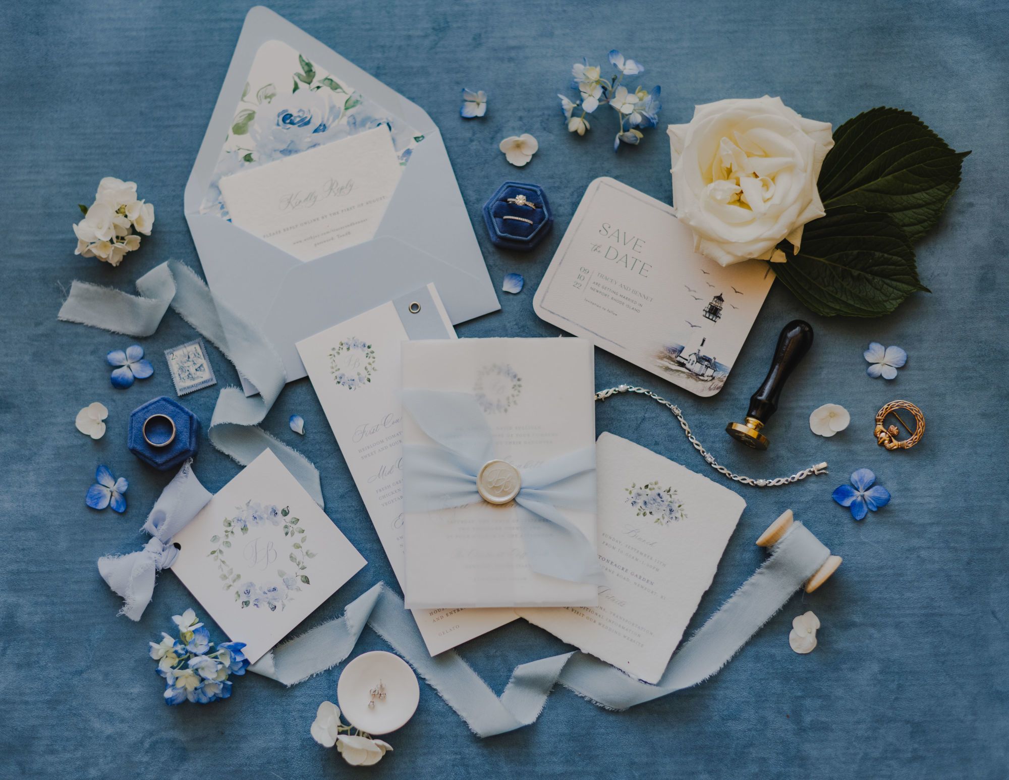 Blue and cream wedding invitations with floral design displayed on a velvet background with ribbon and flowers | PartySlate