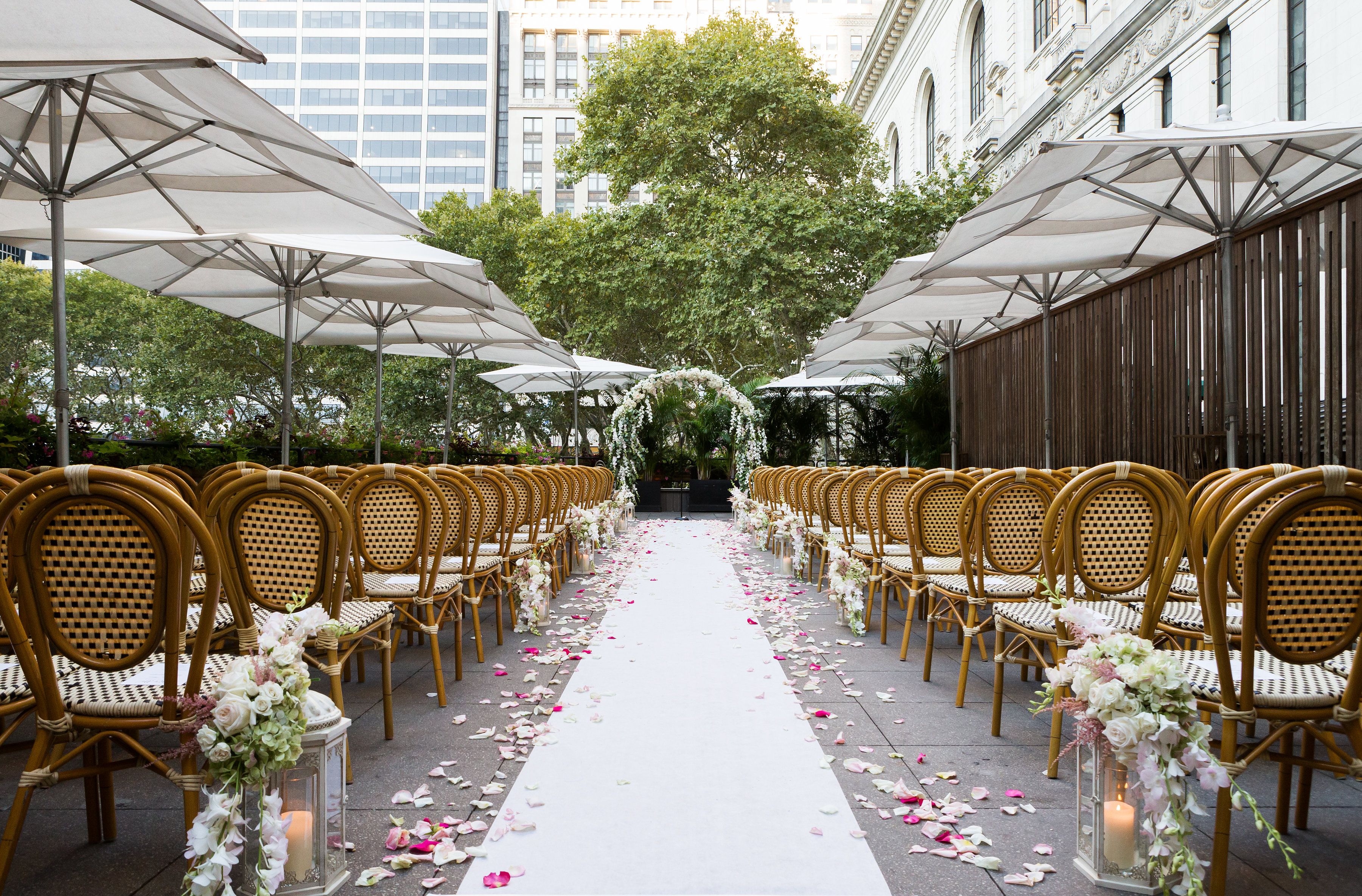 Elegant outdoor wedding ceremony setup with floral aisle, lanterns, and rows of chairs beneath white umbrellas at Bryant Park Grill York